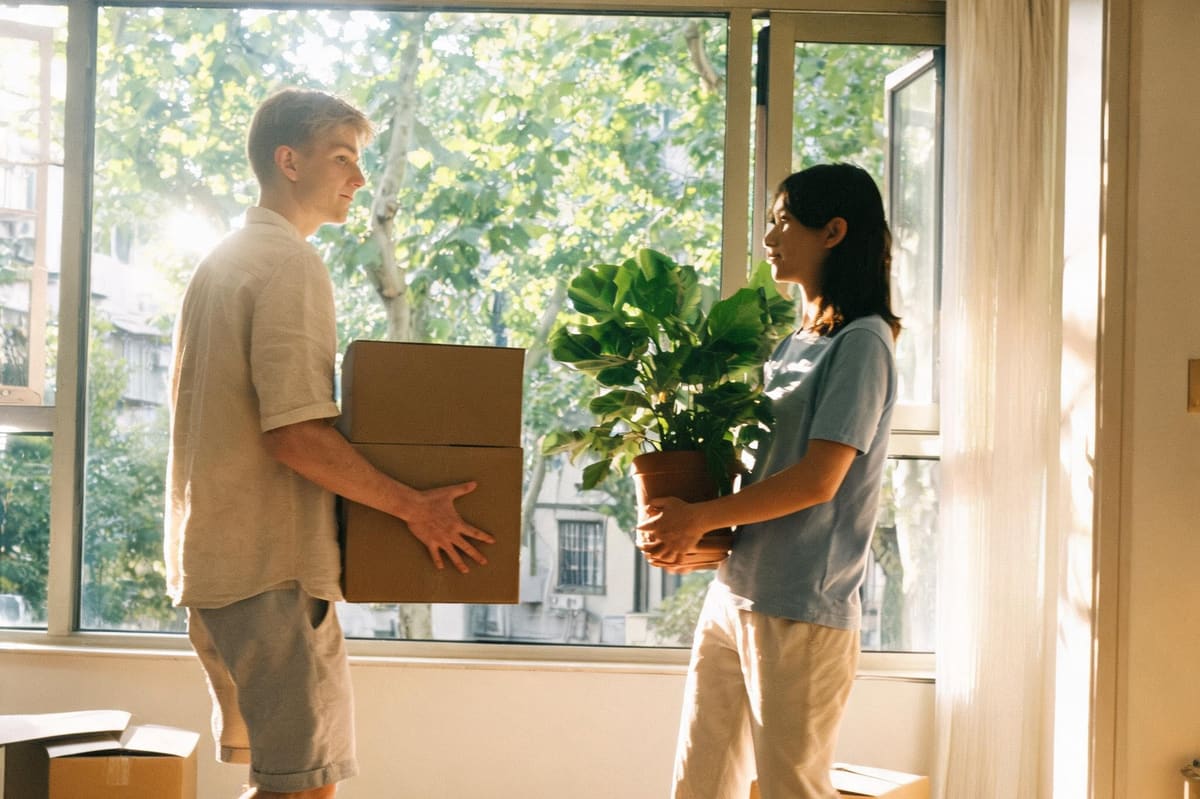 A young couple carrying a moving box and a houseplant into their sunlit new Shanghai apartment