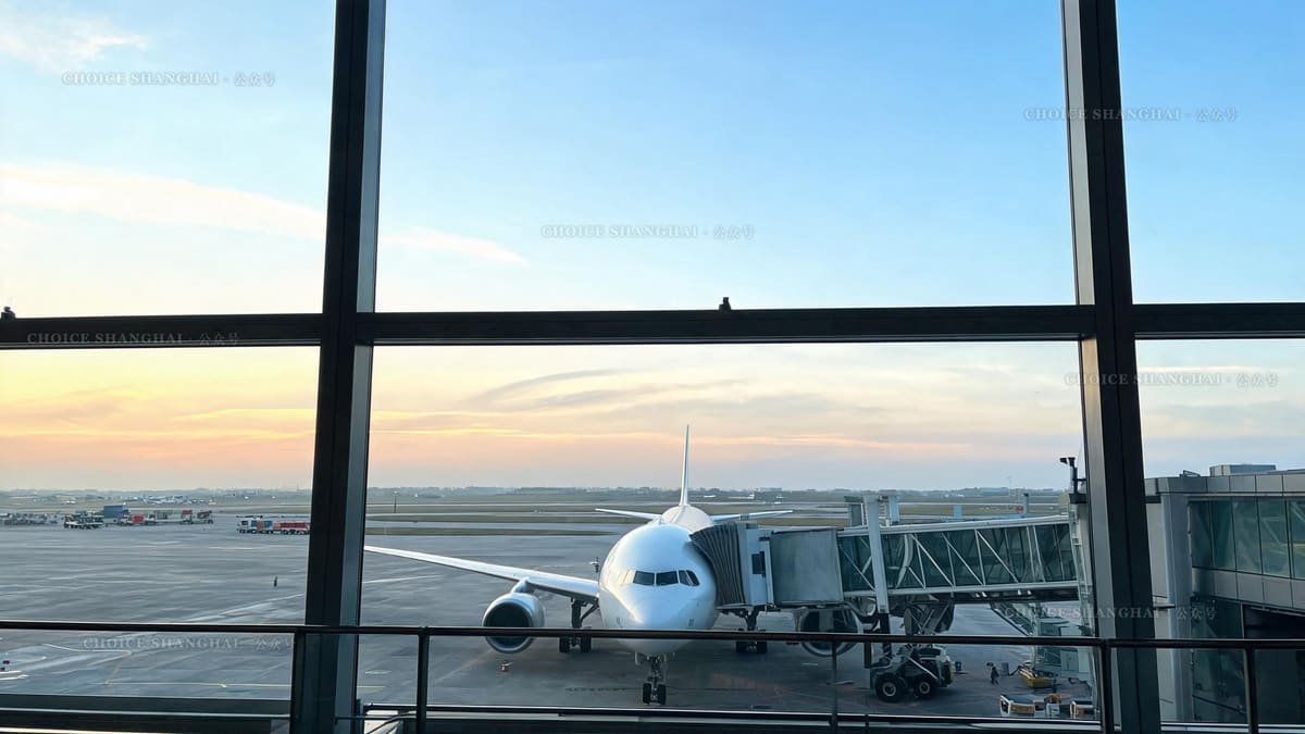 A passenger jet parked at the jet bridge seen through a wide Shanghai airport terminal window at dawn