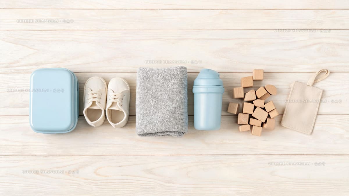 A flat lay of nursery daily items in Shanghai: a small lunchbox, tiny shoes, a folded towel, a sippy cup and wooden blocks