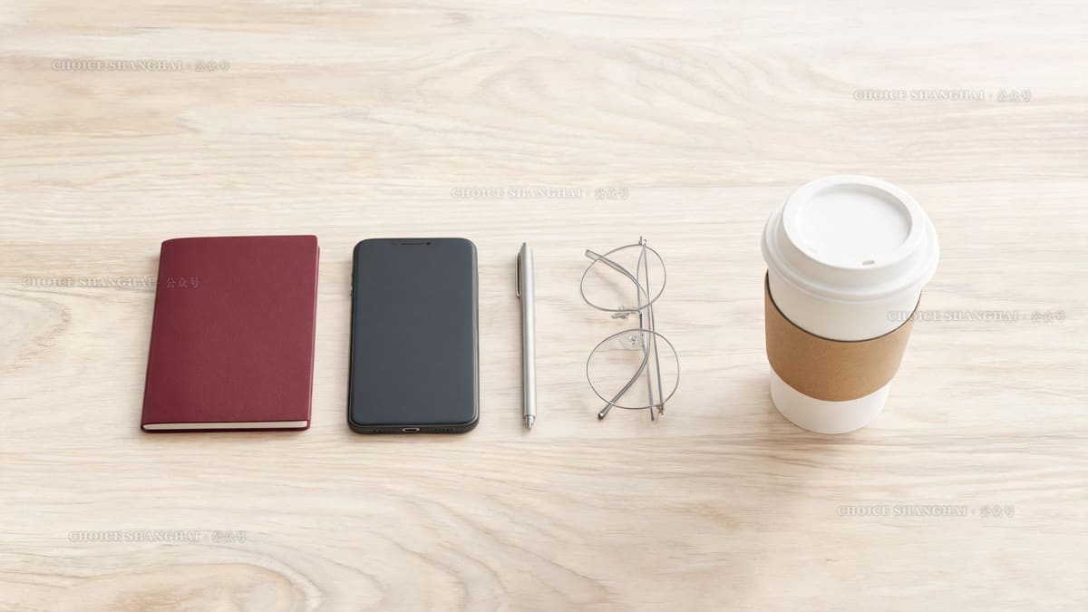 Overhead flat lay of a burgundy passport, phone, pen and glasses on a pale wood counter before a visa appointment in Shanghai