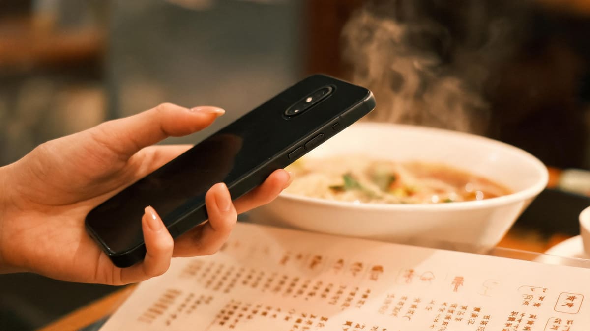 Close up of a hand holding a smartphone over a Chinese restaurant menu, the phone camera p