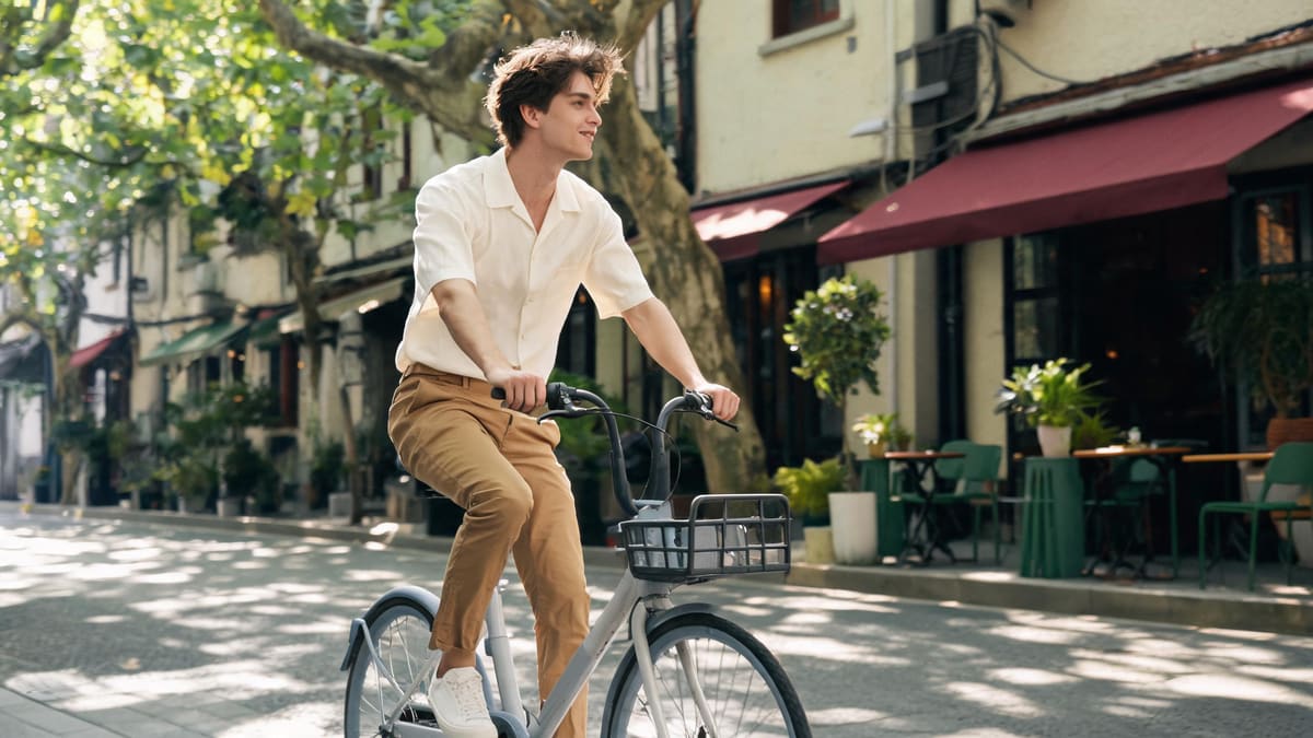 Rider on a shared city bike coasting down a leafy tree-lined Shanghai lane past a cafe