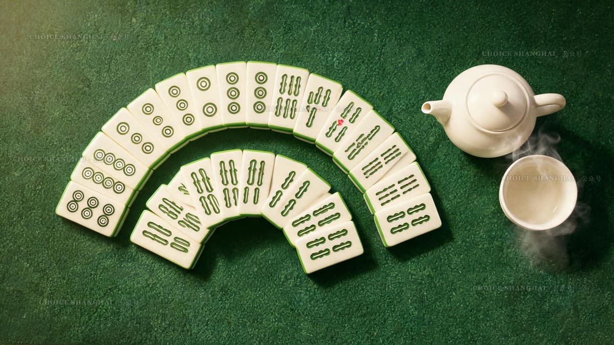 A completed mahjong hand of circle and bamboo tiles fanned on green felt beside a steaming teapot in a Shanghai teahouse
