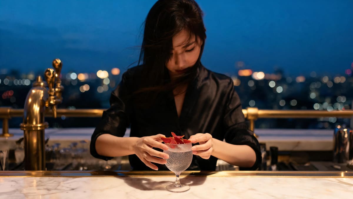 A bartender finishing a cocktail at a high rooftop bar counter at blue hour 蓝调时刻,高层露台吧台上调酒收尾