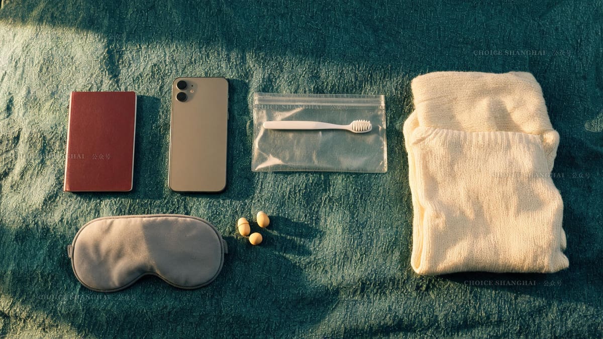 Overnight packing kit on green linen: passport, phone, toothbrush pouch, eye mask, earplugs and a folded cream sweater