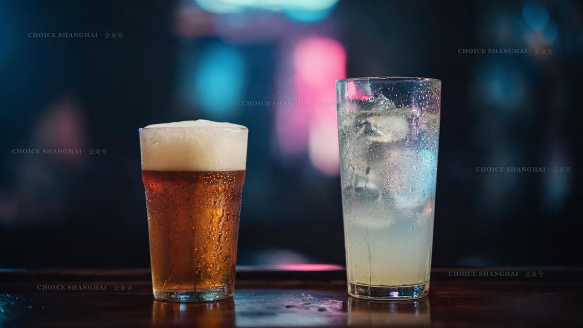 A craft beer and a tall highball on a dim Shanghai bar counter with a soft neon glow behind