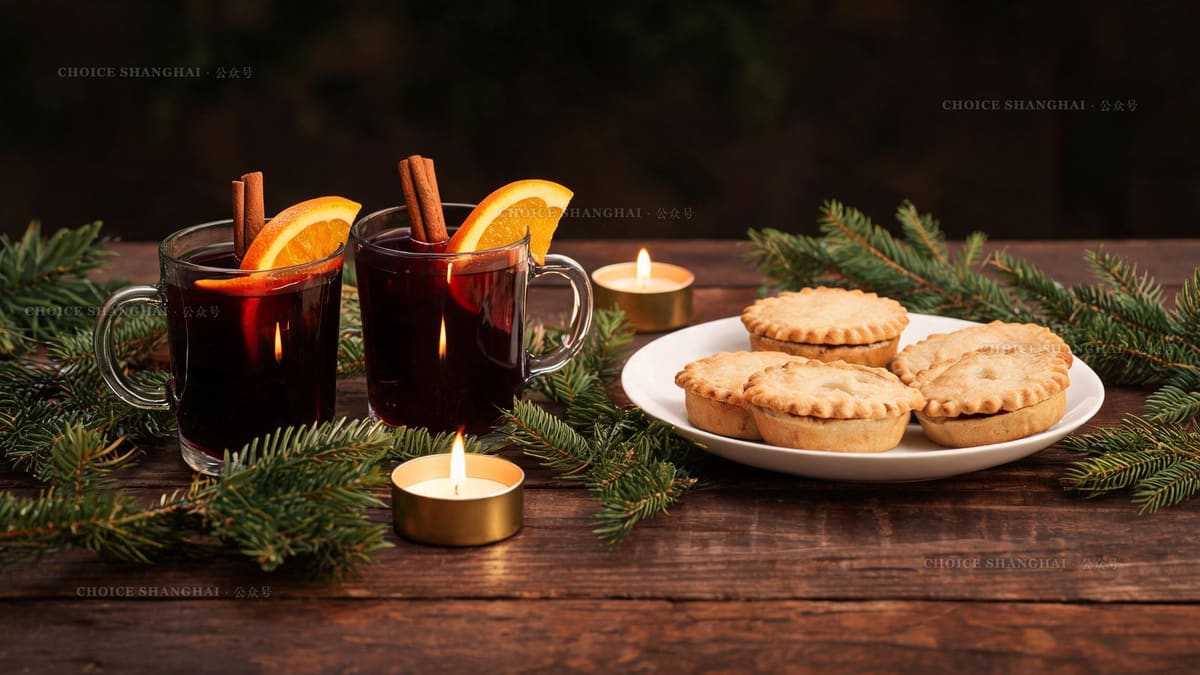 Two glasses of mulled wine with orange and cinnamon beside a plate of mince pies and pine sprigs at a Shanghai Christmas market