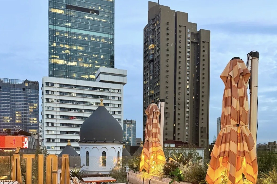 Ática's rooftop terrace at golden hour, striped umbrellas and rattan chairs, with a church dome and the city skyline behind