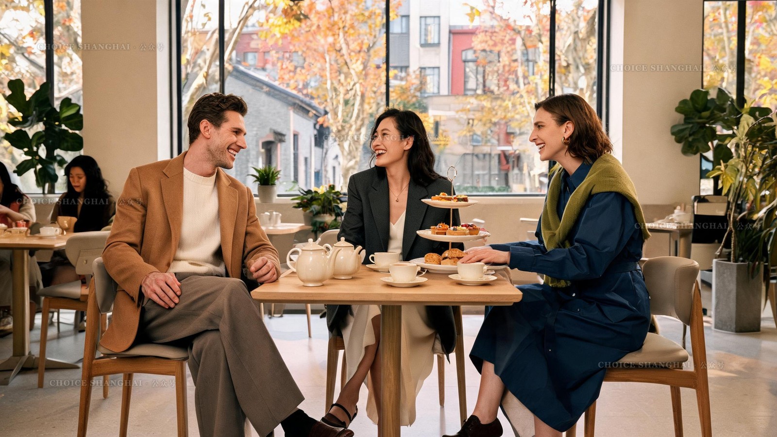 Three friends laughing over a two-tier afternoon tea set and pots of tea at a bright Shanghai cafe with autumn trees outside