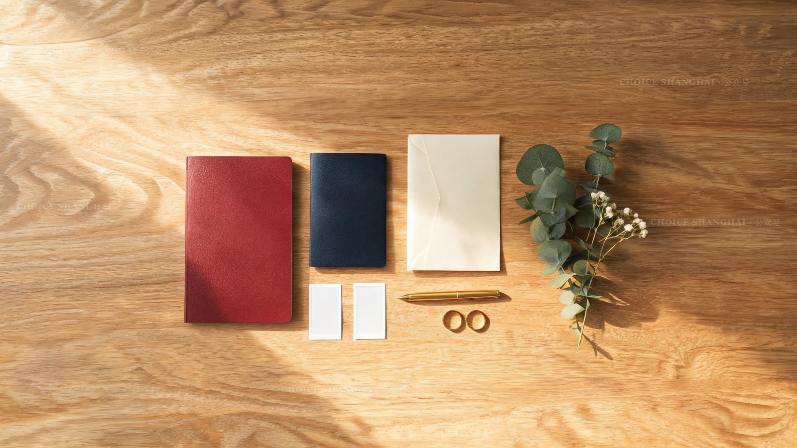 Flat lay of marriage paperwork: a red certificate booklet, passport, photo prints, gold pen and wedding rings on a warm desk