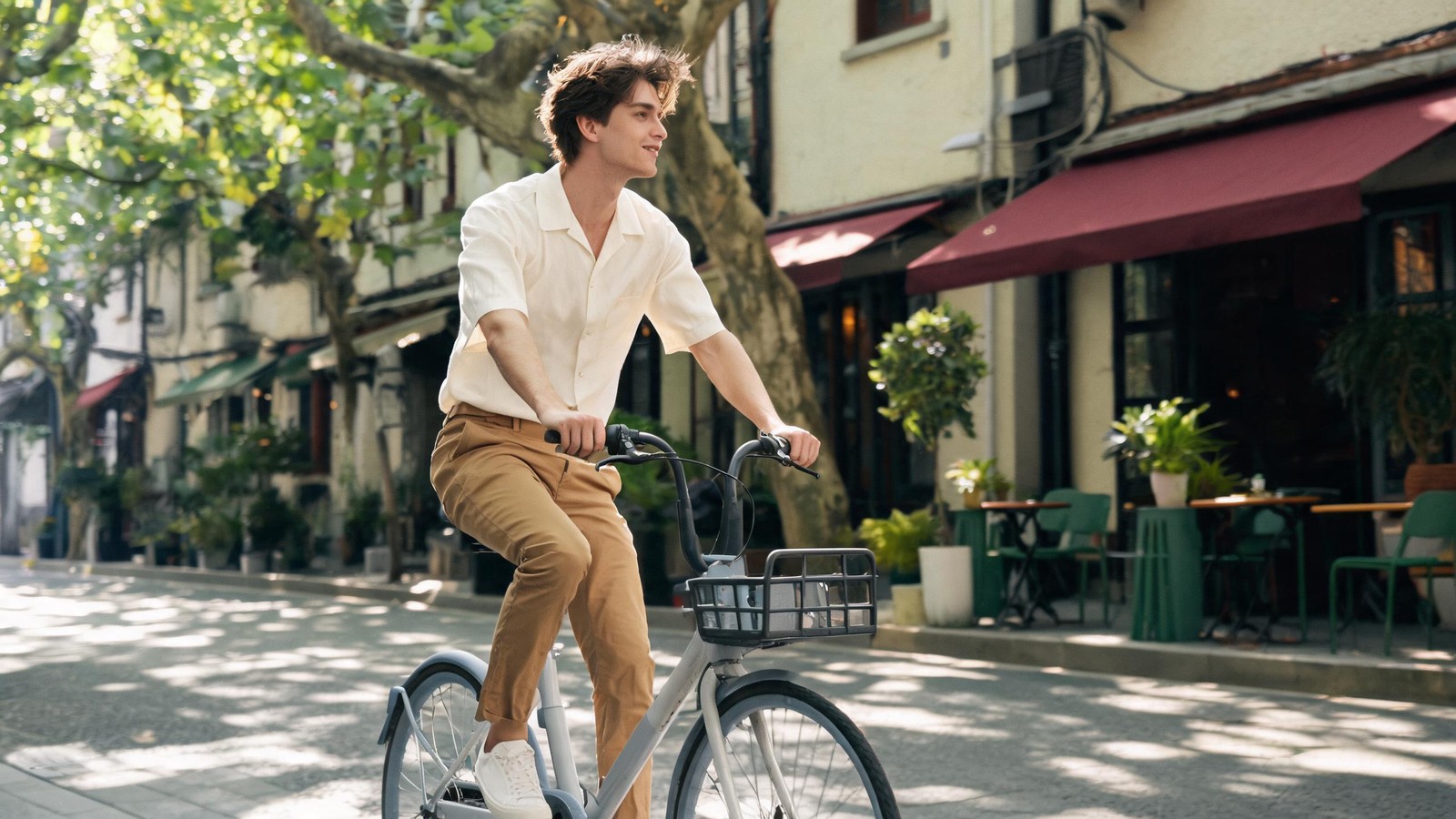 Rider on a shared city bike coasting down a leafy tree-lined Shanghai lane past a cafe