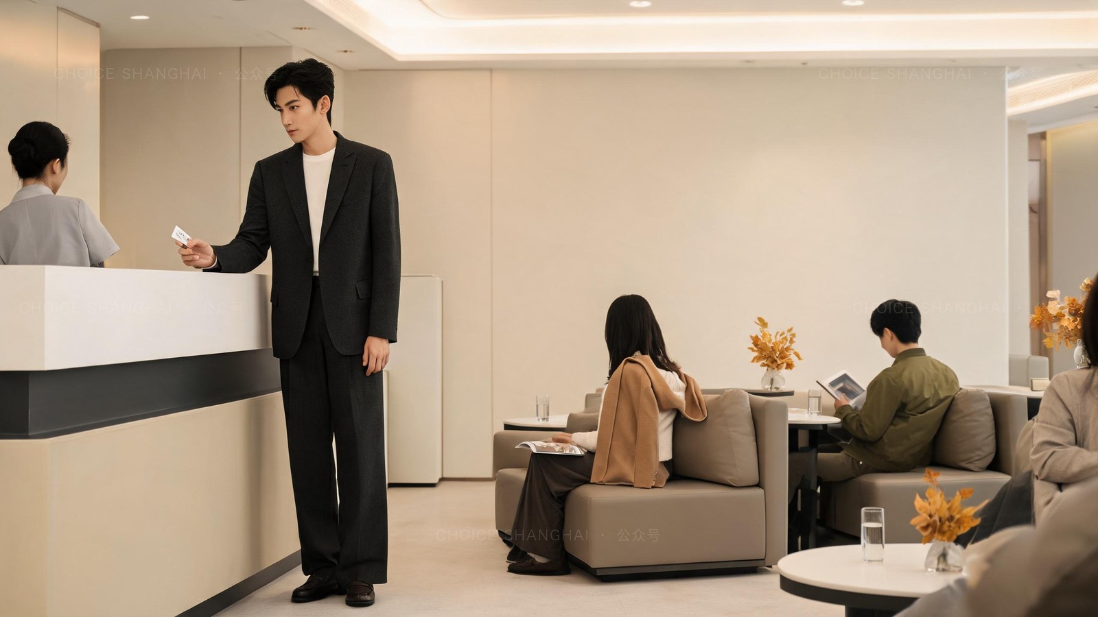 A man in a charcoal blazer checking in at a quiet VIP international reception counter in a Shanghai public hospital, calm lounge with seated patients turned away