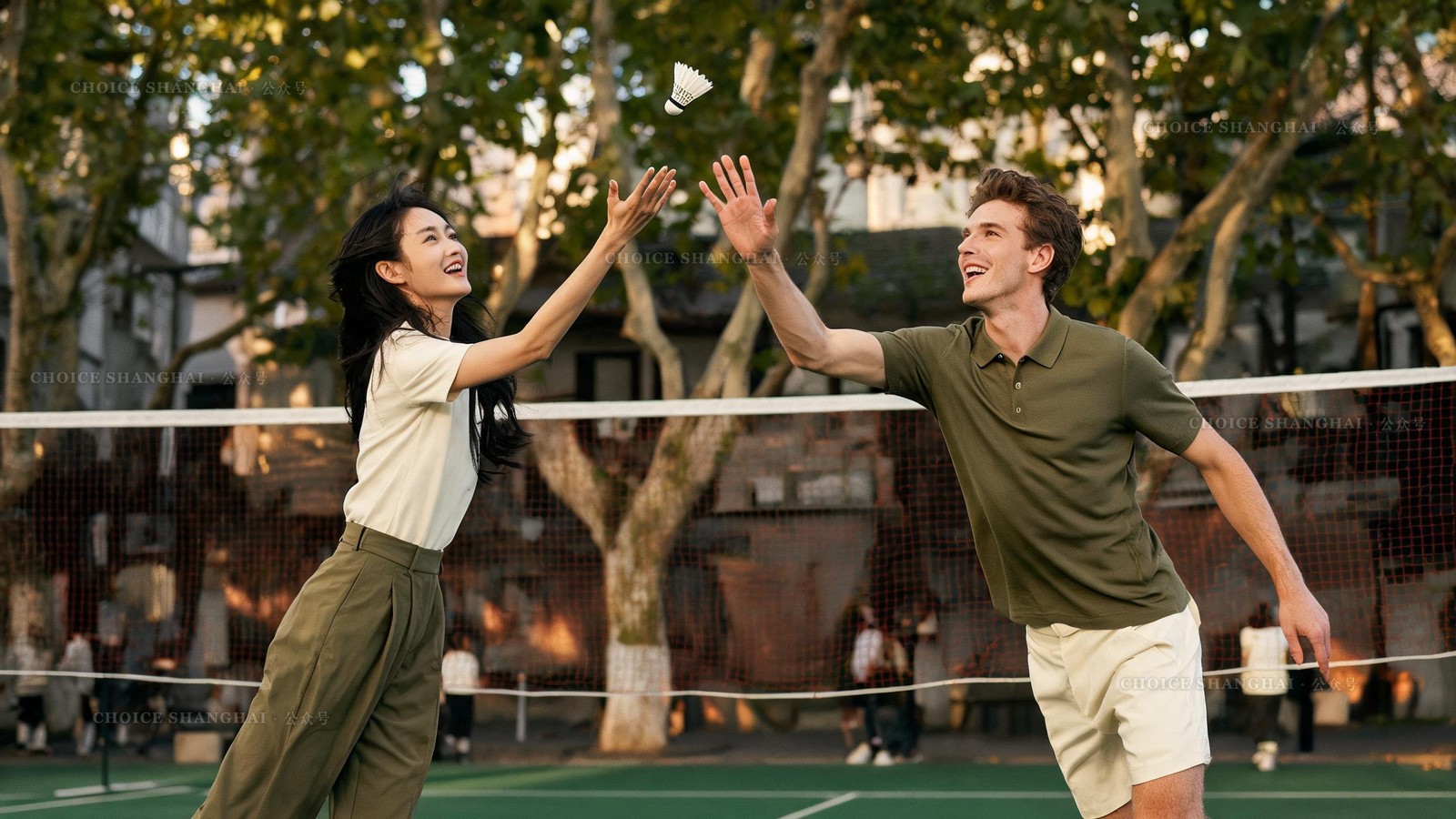 An East Asian woman and a European man laughing over a casual weekend badminton meetup on a Shanghai community court in early autumn
