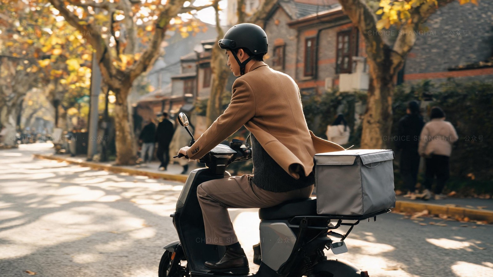 An errand courier riding an electric scooter with a plain insulated box down a tree-lined Shanghai street with yellowing autumn leaves