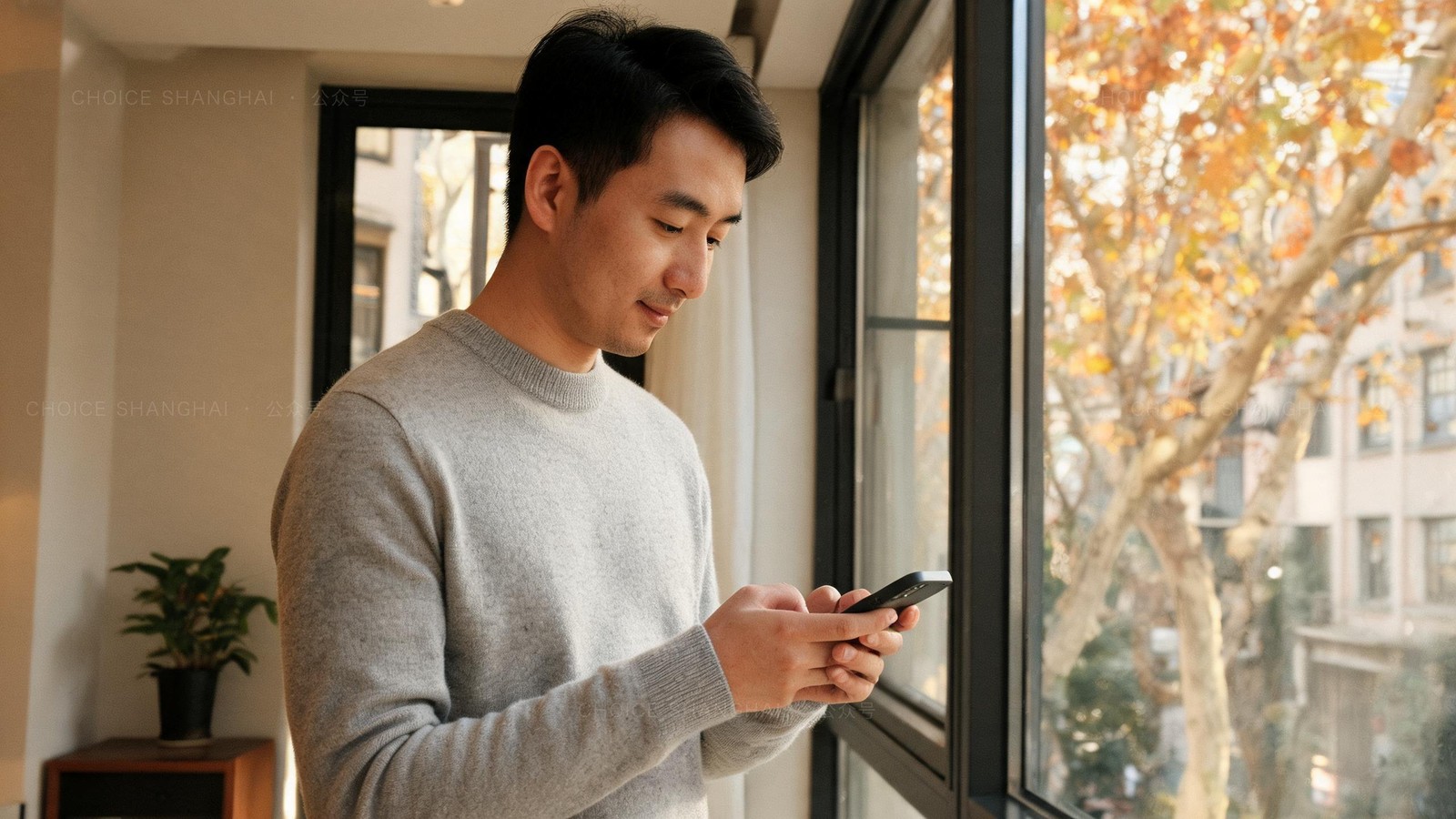 An expat checking his banking app by a window in a Shanghai apartment with autumn trees outside