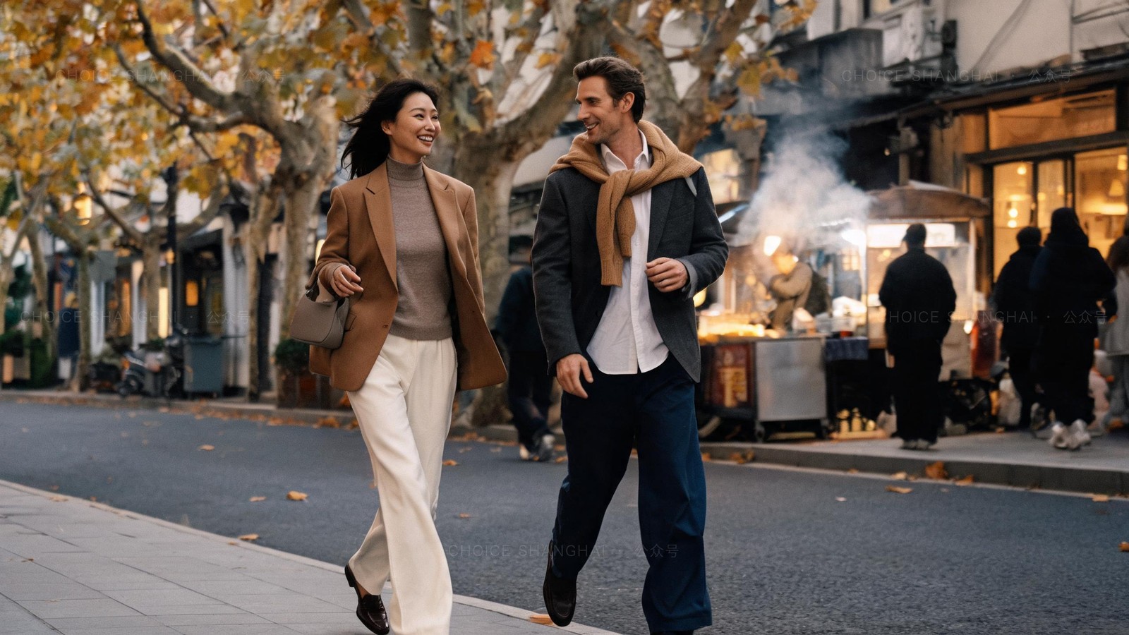 Two friends walking and laughing along a leafy Xuhui street in autumn with a street-food stall behind them