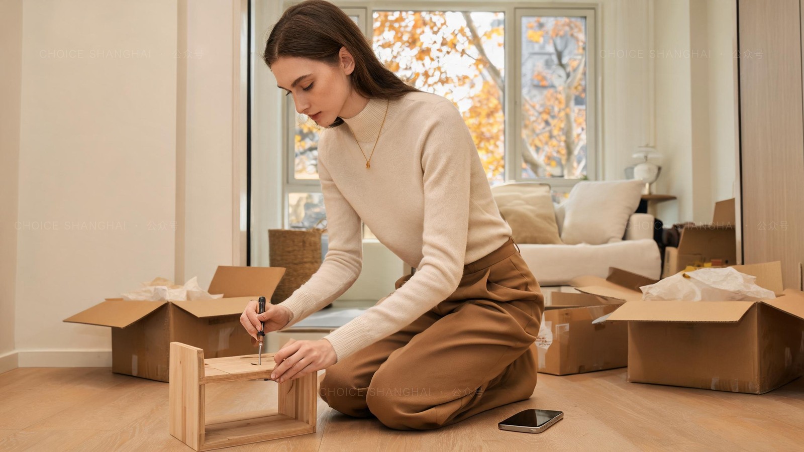 A young expat woman assembling a second-hand wooden shelf among opened delivery parcels in a bright Shanghai flat, the cheap way to furnish a first apartment