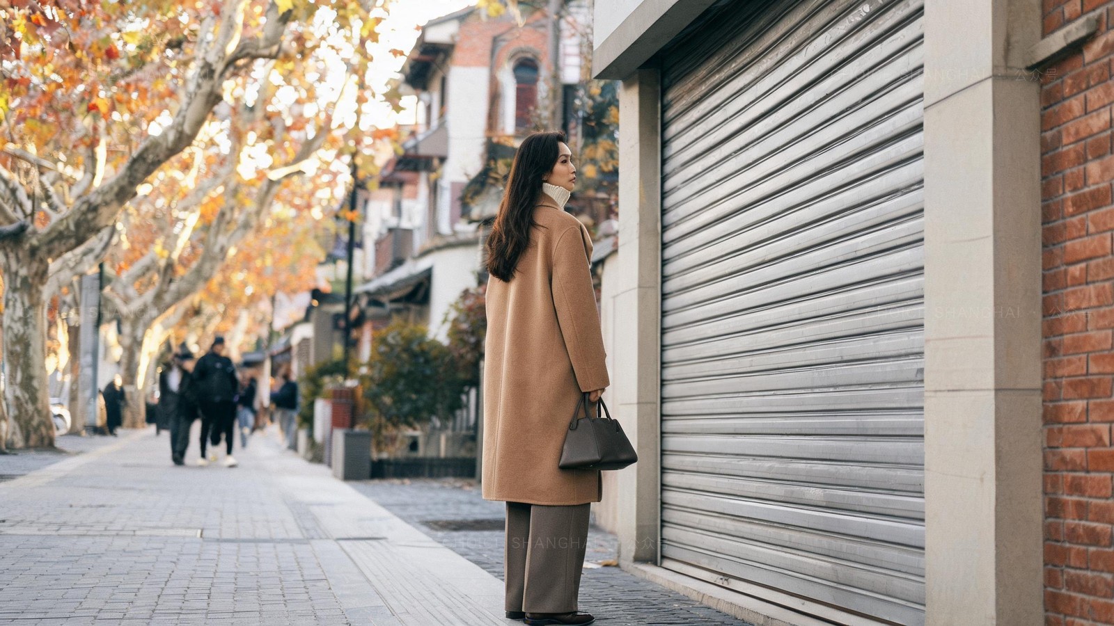 A person standing outside a small Shanghai storefront with the metal shutter pulled down on an autumn afternoon