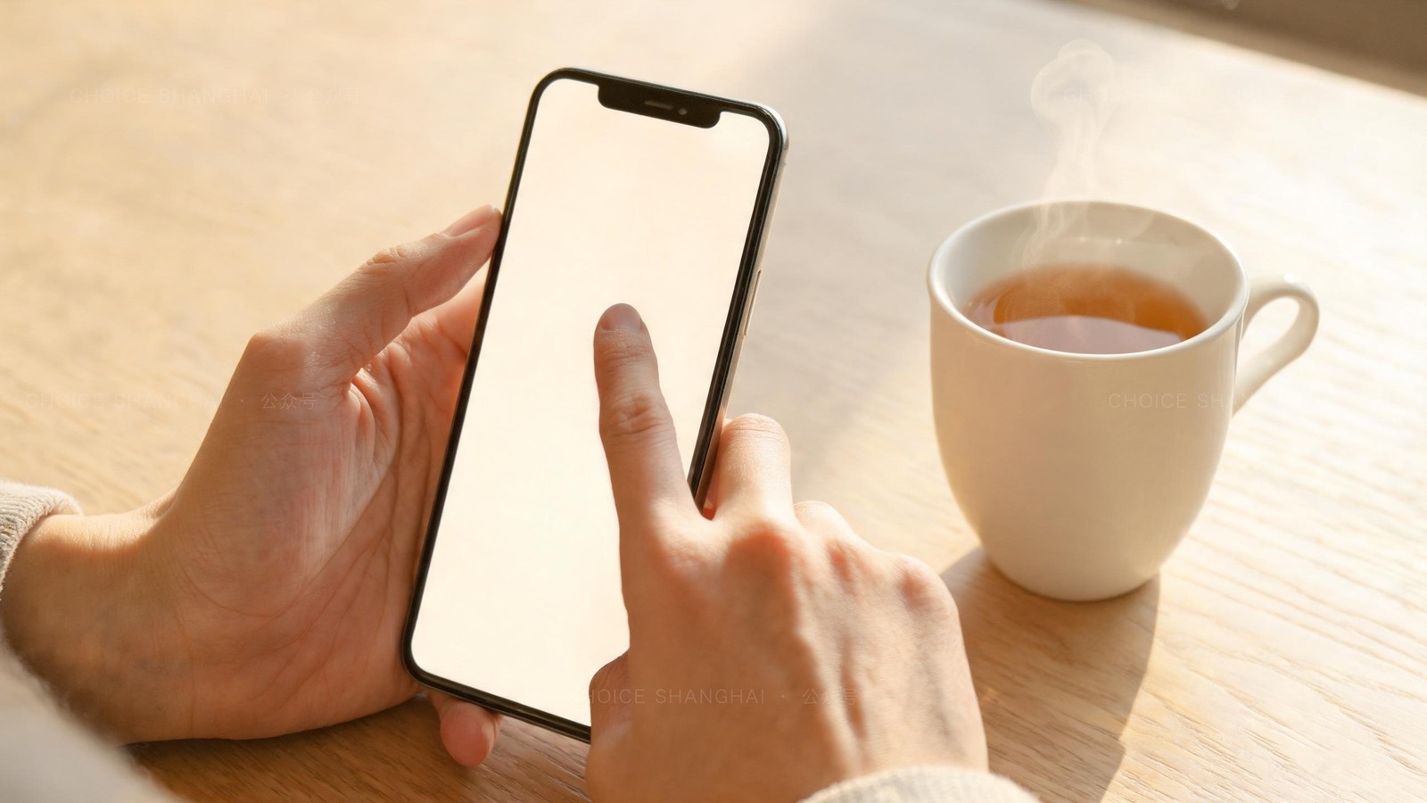Two hands holding a smartphone and scrolling a settings screen beside a cup of tea on a pale wooden table in warm daylight