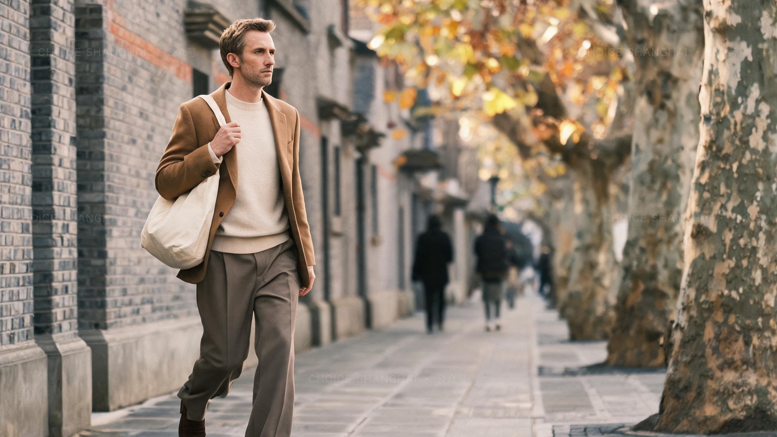 A man in a camel coat walking alone mid-stride down a quiet Shanghai lane with a canvas tote on an autumn morning