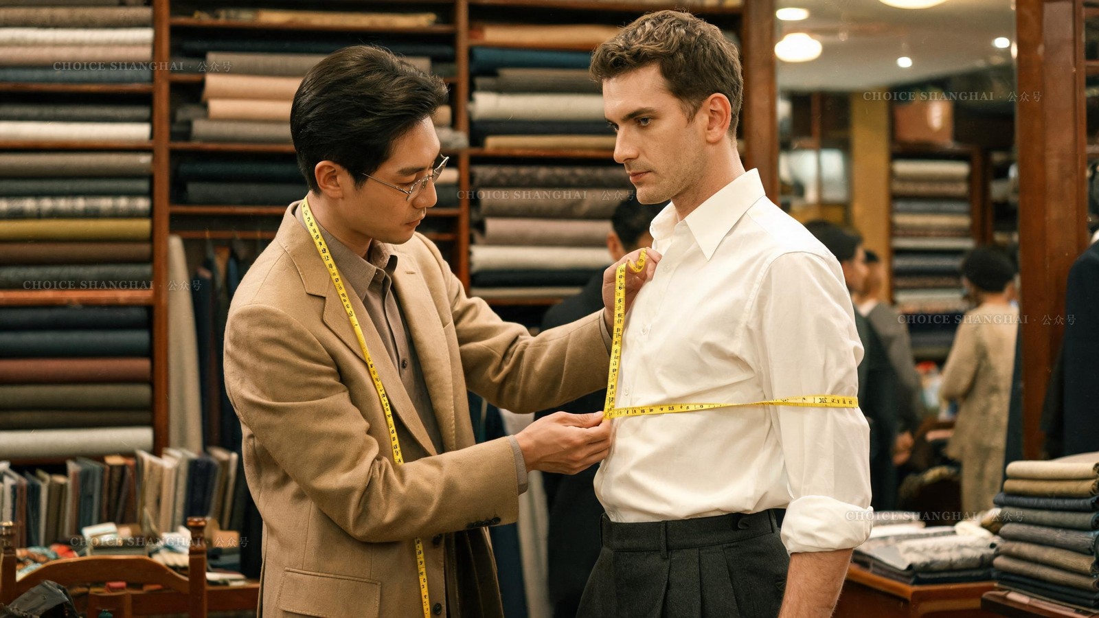 Shanghai tailor measuring a customer's chest with a tape measure beside bolts of wool at a fabric market